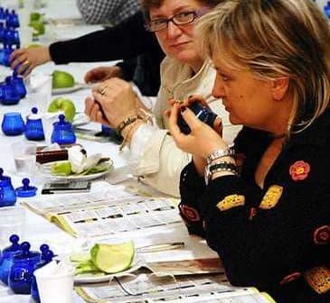 Two women participating in an olive oil tasting event, examining samples at a table. - Olive Oil Times