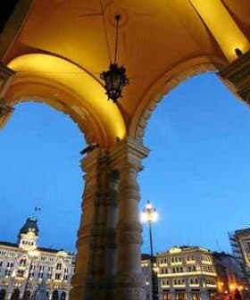 Archway with decorative columns and lanterns, overlooking a city square in Trieste during twilight. - Olive Oil Times
