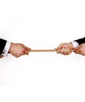 Two hands in business suits gripping a rope from opposite ends, engaged in a tug-of-war. - Olive Oil Times
