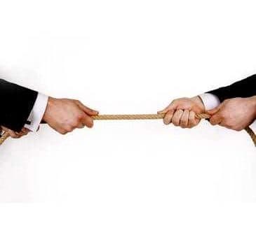 Two hands in business suits gripping a rope from opposite ends, engaged in a tug-of-war. - Olive Oil Times