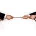 Two hands in business suits gripping a rope from opposite ends, engaged in a tug-of-war. - Olive Oil Times