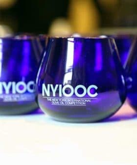 Set of blue glasses featuring the logo of the New York International Olive Oil Competition. - Olive Oil Times