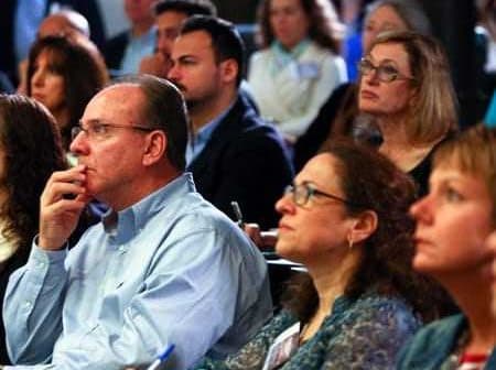 A diverse group of individuals attentively listening during a conference presentation. - Olive Oil Times