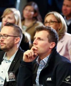 Two men in the foreground listening attentively during an event with an audience in the background. - Olive Oil Times