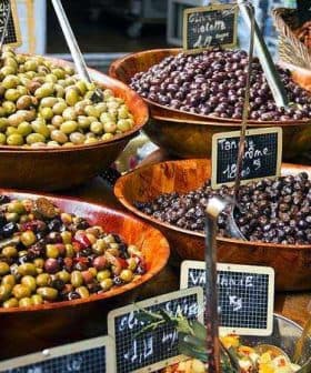 Multiple wooden bowls filled with different types of olives displayed at a market. - Olive Oil Times