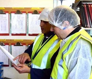 Two workers in safety vests and hairnets examining a document in a workplace setting. - Olive Oil Times