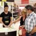 A young man serving olive oil samples to two customers in a store aisle. - Olive Oil Times