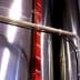 Close-up of a stainless steel storage tank with a measurement scale and piping. - Olive Oil Times