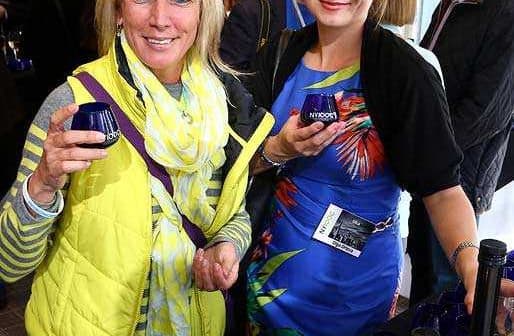 Two women holding glasses at a social event, one wearing a yellow vest and the other in a floral dress. - Olive Oil Times