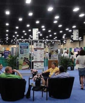 Exhibition hall with attendees seated in chairs and various displays in the background. - Olive Oil Times