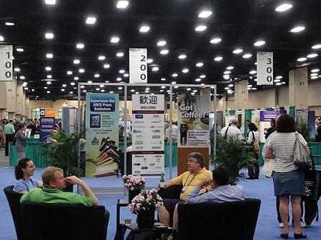Exhibition hall with attendees seated in chairs and various displays in the background. - Olive Oil Times