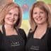 Two women wearing black aprons with 'Cleo's' logo, smiling at the camera in a studio setting. - Olive Oil Times