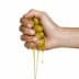 A hand squeezing a cluster of green olives, with olive oil dripping from them. - Olive Oil Times