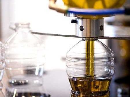 Machine filling plastic bottles with olive oil during the bottling process in a factory. - Olive Oil Times