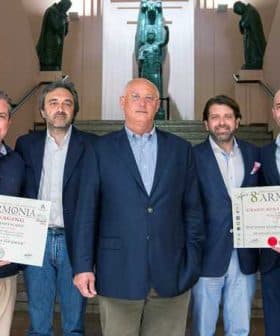 Five individuals posing together at an event, holding certificates in front of a sculpture backdrop. - Olive Oil Times
