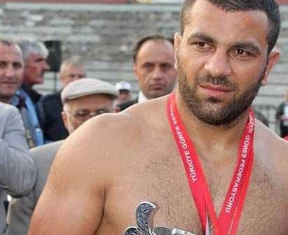 A shirtless wrestler holding a trophy while wearing a medal around his neck. - Olive Oil Times