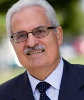 A man wearing glasses and a suit, smiling at the camera in an outdoor setting. - Olive Oil Times