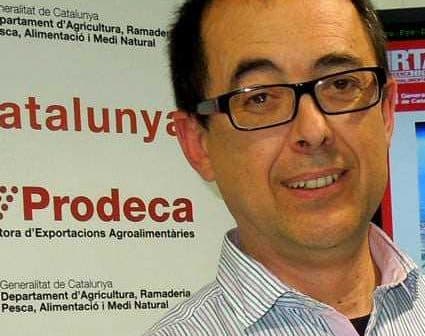 Man wearing glasses smiling at an event with Prodeca branding in the background. - Olive Oil Times
