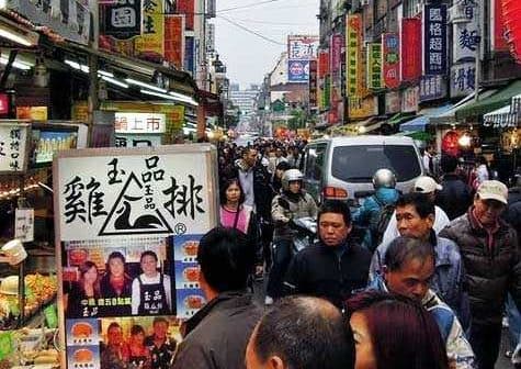 Crowd of people walking through a bustling street market in Taiwan with various stalls and signage. - Olive Oil Times