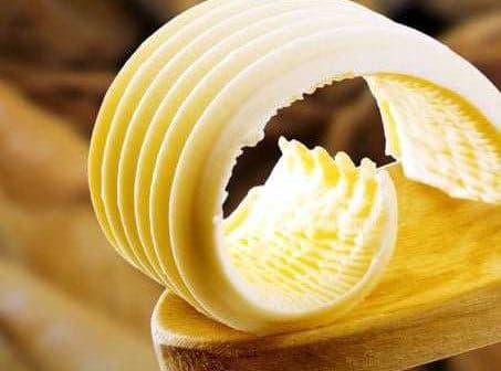 Slices of butter arranged on a wooden spoon with a smooth texture. - Olive Oil Times