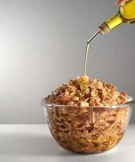 A glass bowl filled with cereal being drizzled with olive oil from a bottle. - Olive Oil Times