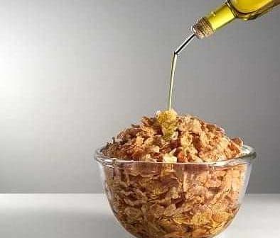 A glass bowl filled with cereal being drizzled with olive oil from a bottle. - Olive Oil Times