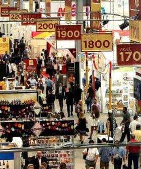 View of aisles at a food trade show with signage indicating aisle numbers and various booths. - Olive Oil Times