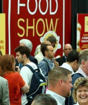 Crowd of attendees at a food show event with a large red banner in the background. - Olive Oil Times