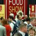 Crowd of attendees at a food show event with a large red banner in the background. - Olive Oil Times