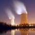 Two cooling towers emitting steam at night with reflections on the water surface. - Olive Oil Times