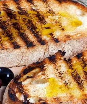Two slices of grilled bread topped with olive oil and grill marks on a wooden board. - Olive Oil Times