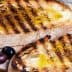 Two slices of grilled bread topped with olive oil and grill marks on a wooden board. - Olive Oil Times