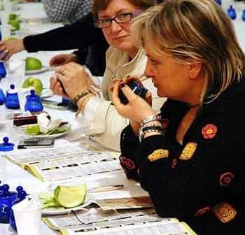 Two women participating in an olive oil tasting event, with green apples and blue tasting cups on the table. - Olive Oil Times
