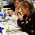 Two women participating in an olive oil tasting event, with green apples and blue tasting cups on the table. - Olive Oil Times