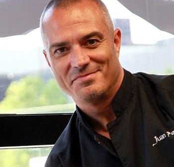 Portrait of a chef named Juan Pablo wearing a black chef's jacket and smiling at the camera. - Olive Oil Times