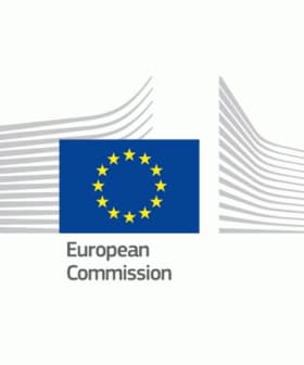 Logo of the European Commission featuring a blue background with yellow stars and stylized building outlines. - Olive Oil Times