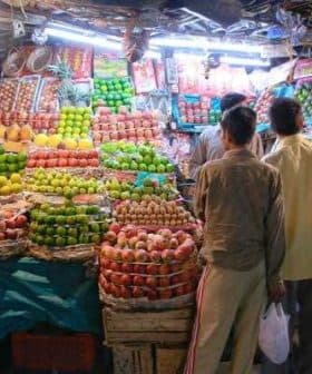 Two individuals observing a fruit stall filled with various types of apples and other fruits in baskets. - Olive Oil Times