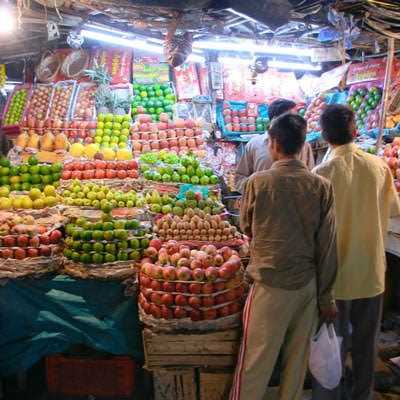 Two individuals observing a fruit stall filled with various types of apples and other fruits in baskets. - Olive Oil Times