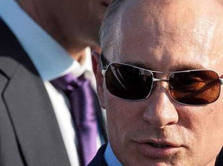 Man wearing sunglasses and a suit, with a blurred figure in the background. - Olive Oil Times