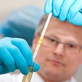 Scientist in gloves examining a test tube with a colorimetric analysis strip for measurement. - Olive Oil Times
