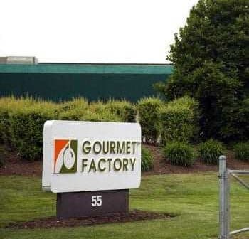 Sign for Gourmet Factory located at 55, featuring a logo and text on a white background. - Olive Oil Times