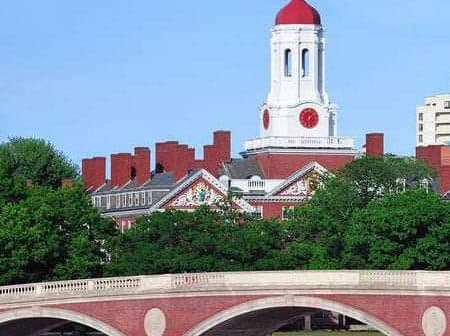 Harvard University building featuring a red dome and clock tower, viewed from across the river. - Olive Oil Times