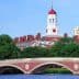 Harvard University building featuring a red dome and clock tower, viewed from across the river. - Olive Oil Times