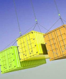 Three shipping containers in yellow, green, and orange suspended from cables against a blue sky. - Olive Oil Times