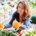 Woman holding two yellow bell peppers while shopping at a market filled with various vegetables. - Olive Oil Times