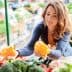 Woman examining yellow bell peppers while shopping at a market stall filled with vegetables. - Olive Oil Times