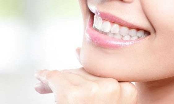 Close-up of a woman's face showing a smile with white teeth and clear skin. - Olive Oil Times