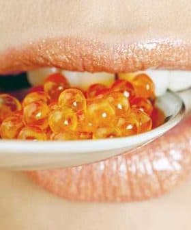 Close-up of a person's mouth holding a spoon with orange caviar beads. - Olive Oil Times