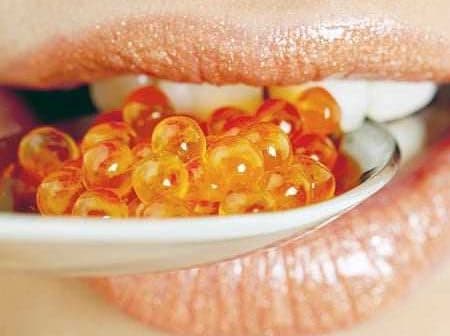 Close-up of a person's mouth holding a spoon with orange caviar beads. - Olive Oil Times