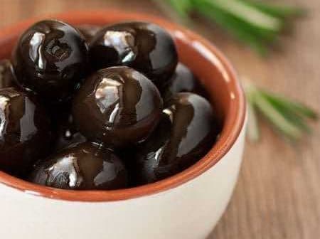 A small bowl filled with black olives placed on a wooden surface. - Olive Oil Times